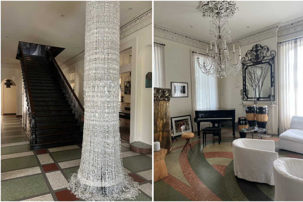 Side-by-side images of the entry to The Kingsway in New Orleans. Left: a wide staircase with a dramatic floor-to-ceiling crystal chandelier and mosaic tile floors. Right: a bright living room with a black grand piano, white slipcovered chairs, modern chandelier, and swirling terrazzo floor.
