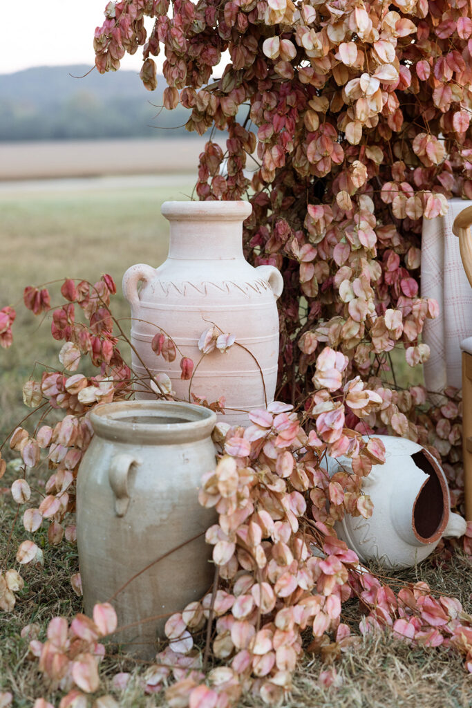 Editorial fall wedding detail with Chinese flame tree branches spilling around ivory clay urns and terracotta vessels on the ground.