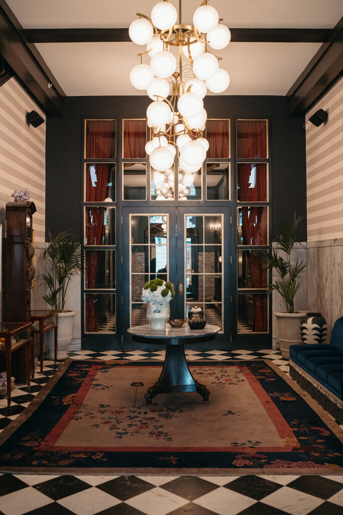 Editorial wedding venue entryway with statement chandelier and checkered floor — showing how lighting and architecture shape atmosphere in wedding design.