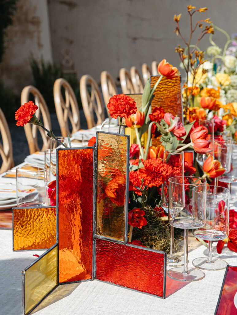 Editorial wedding tablescape featuring stained glass panels, amber tones, and sculptural florals — showcasing layered texture and color in wedding design.