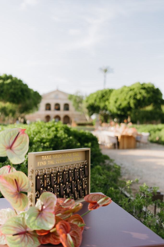 Escort card display with name tags and coral anthurium, the Son Vell manor beyond, Menorca