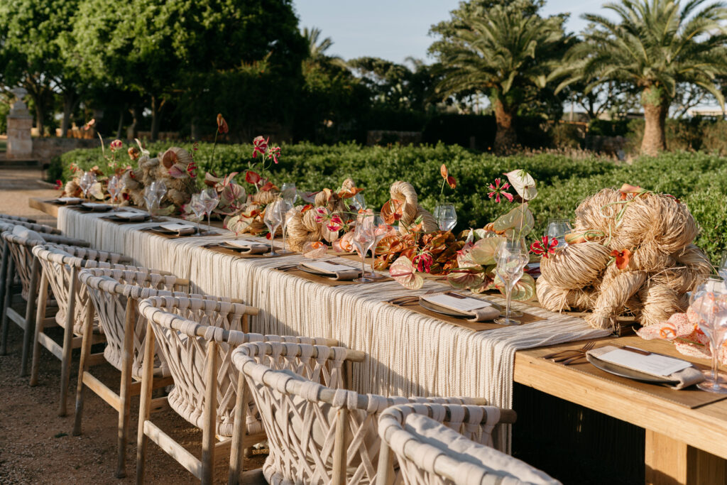 Reception table with a rope, raffia, and coral anthurium runner in the gardens at Son Vell, Menorca