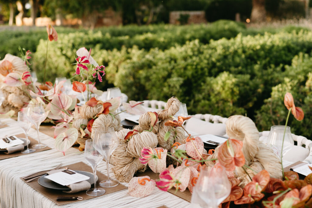 Reception table runner of raffia, coral anthurium and gloriosa in the gardens, Menorca