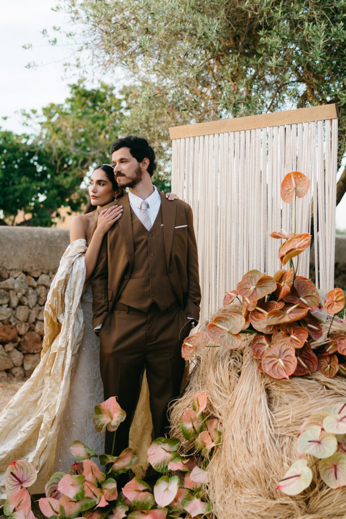 Bride and groom embrace before a woven rope ceremony backdrop with coral anthurium, Son Vell, Menorca
