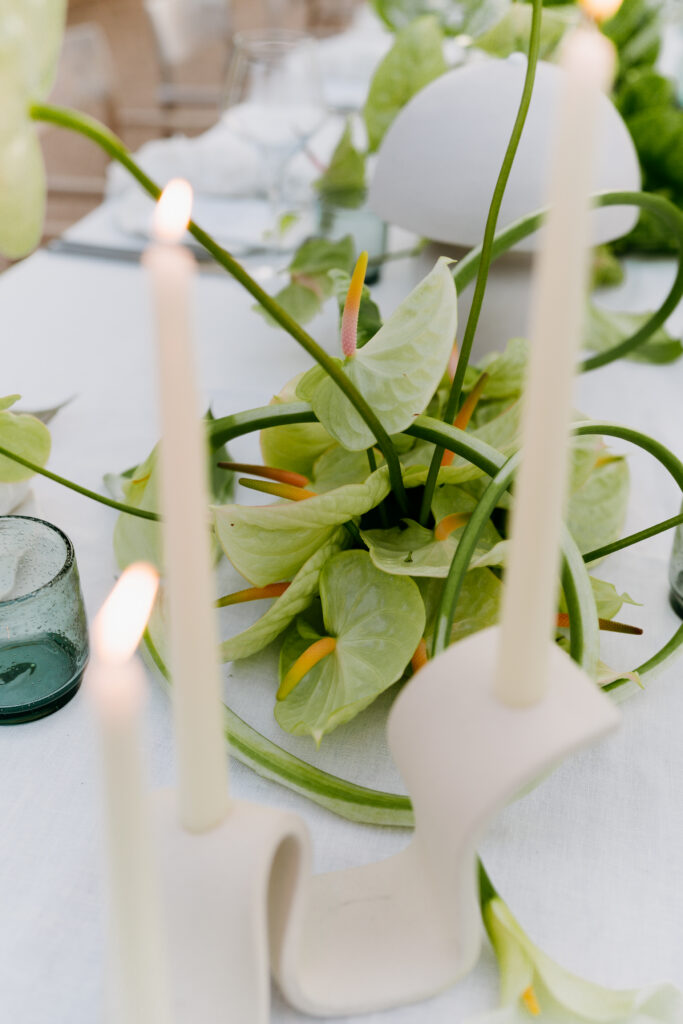 White taper candles and green anthurium centerpiece on a white tablecloth
