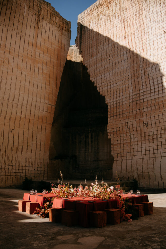 Terracotta wedding tables set on the floor of the Amphitheatre quarry at Lithica, Menorca, dwarfed by 100-foot limestone walls — monochromatic destination wedding designed and produced by Fox & Quinn.