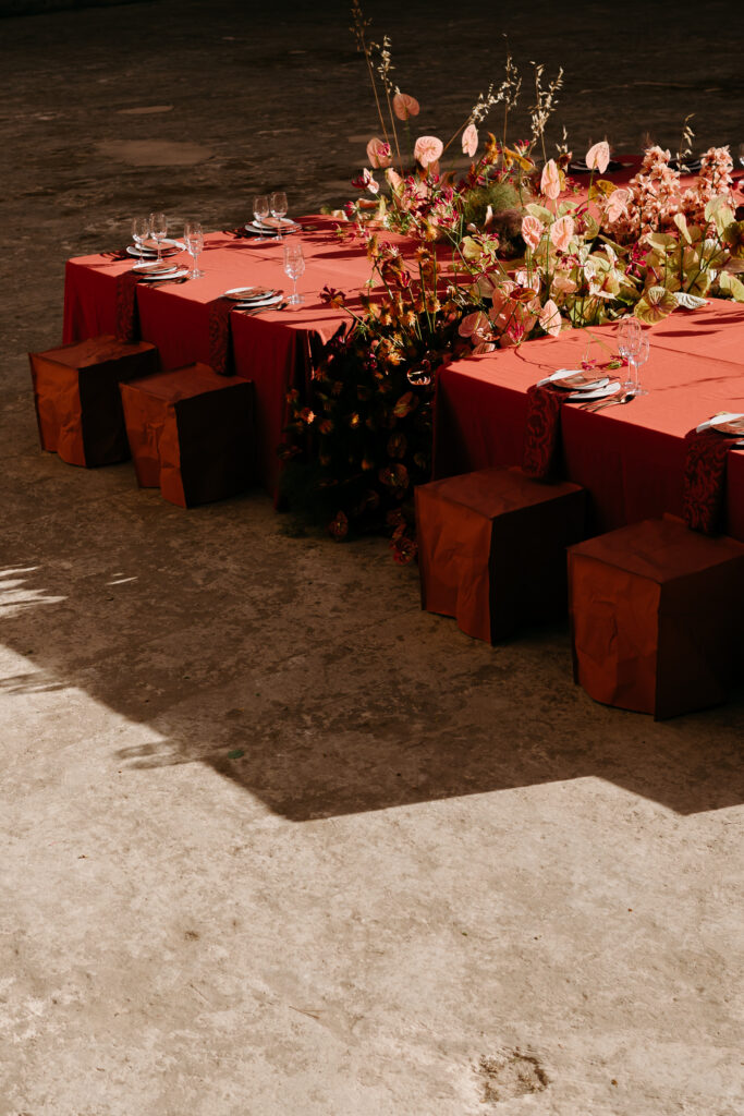 Terracotta wedding tablescape on the quarry floor with anthurium and wild-grass florals and fabric-wrapped cube seating, Lithica Quarry, Menorca — designed and produced by Fox & Quinn.
