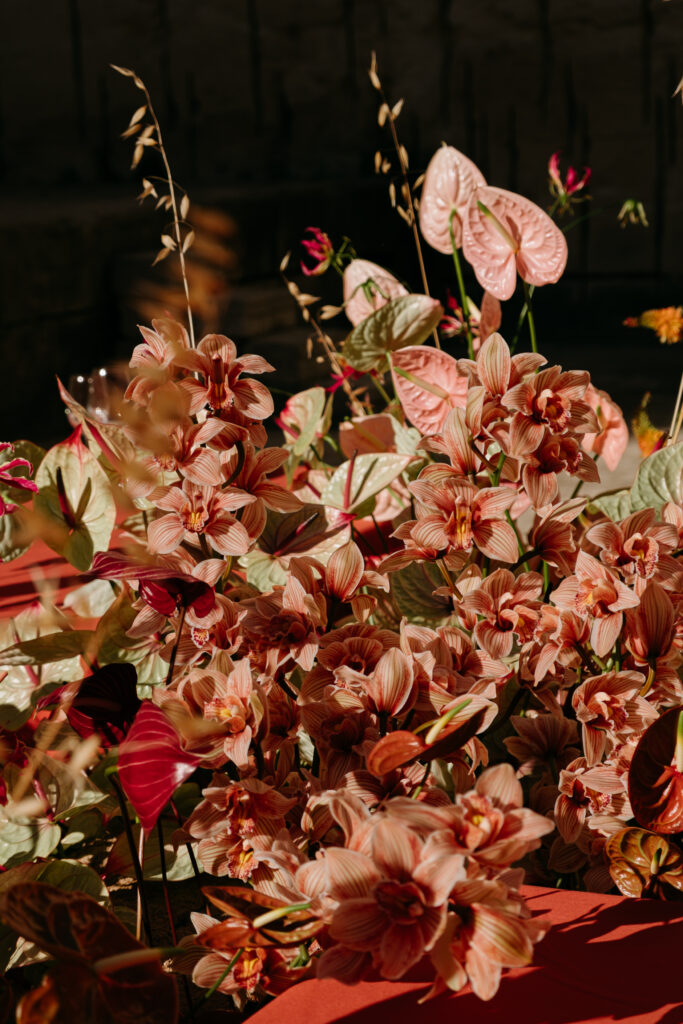 Cascading wedding florals in rust and blush — orchids, anthuriums, and dahlias spilling across terracotta linen at Lithica Quarry, Menorca — designed and produced by Fox & Quinn.