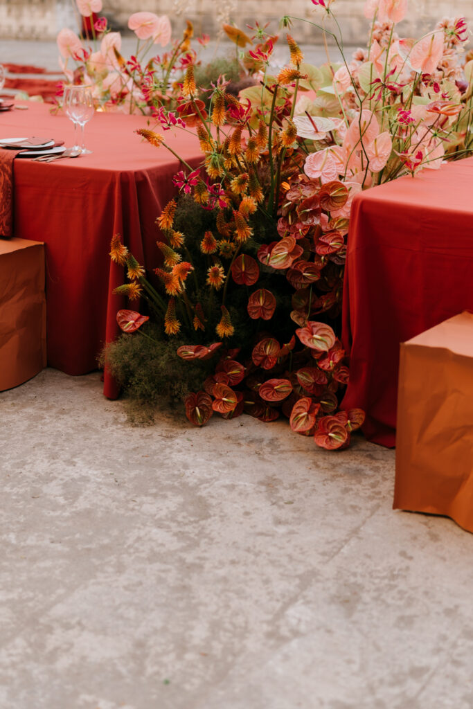 Wedding florals cascading from the terracotta table to the quarry floor — anthuriums, orchids, and kangaroo paw against the stone, Lithica Quarry, Menorca — designed and produced by Fox & Quinn.