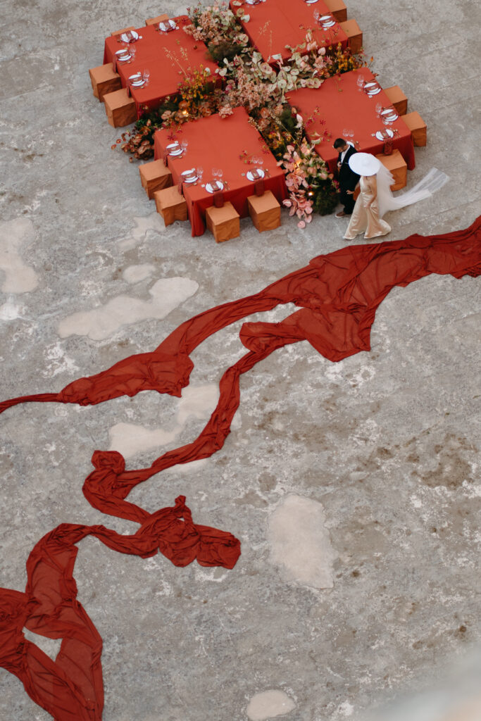 Aerial view of four terracotta wedding tables and the rust chiffon river winding across the quarry floor, Lithica Quarry, Menorca — designed and produced by Fox & Quinn