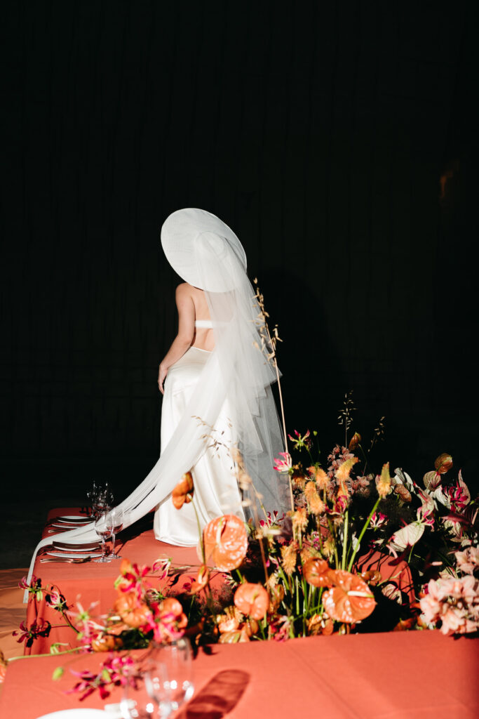 Bride in veil and wide-brimmed hat beside the terracotta table and cascading florals at Lithica Quarry, Menorca
