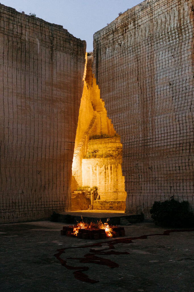 Lithica Quarry at dusk, firelight glowing in the limestone cleft above the rust chiffon river across the stone floor, Menorca — designed and produced by Fox & Quinn.