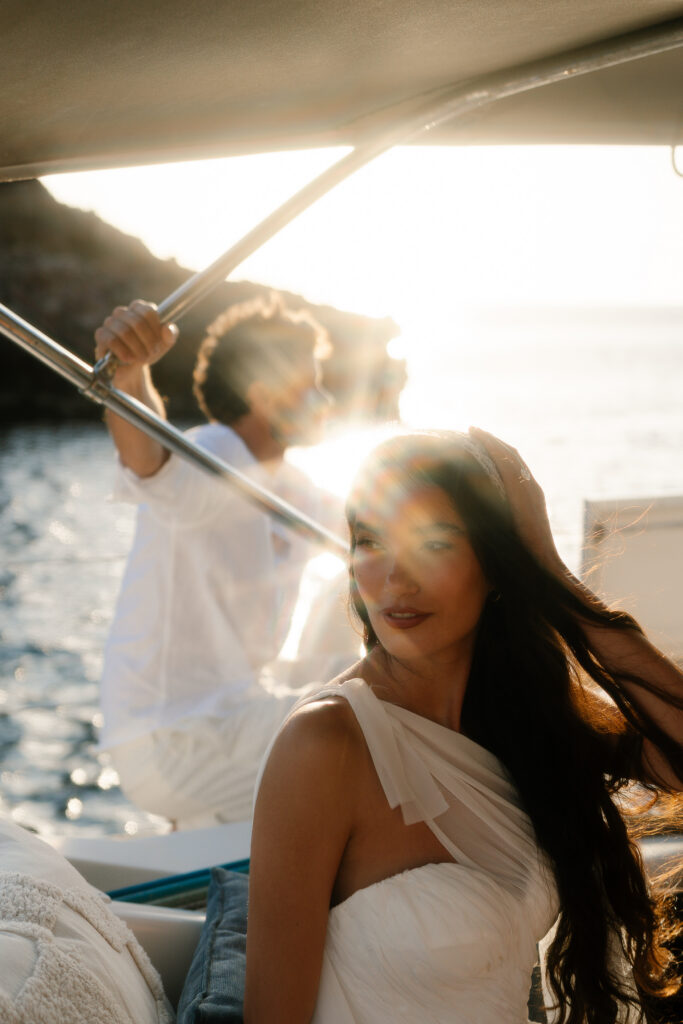 Bride and groom on a boat at golden hour with sun flaring over the Menorca coast