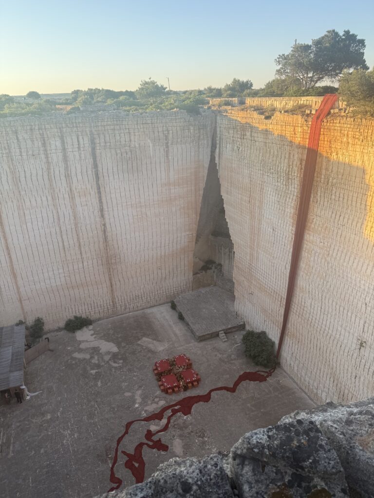 Aerial view of Lithica Quarry, Menorca, with 300 feet of rust chiffon falling down the limestone wall and running across the floor to the terracotta wedding tables — designed and produced by Fox & Quinn.