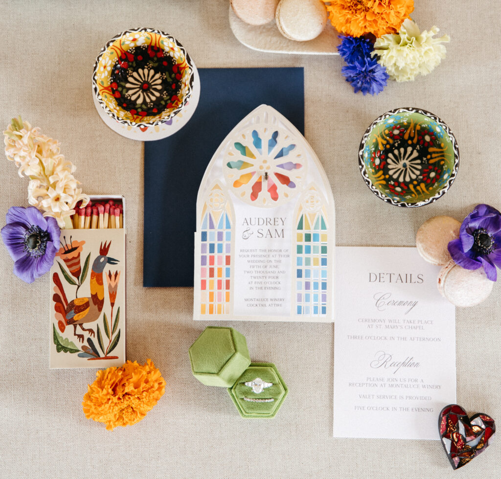 Flatlay featuring a cathedral-inspired invitation suite, European ceramics, and bold florals in a stained glass palette.