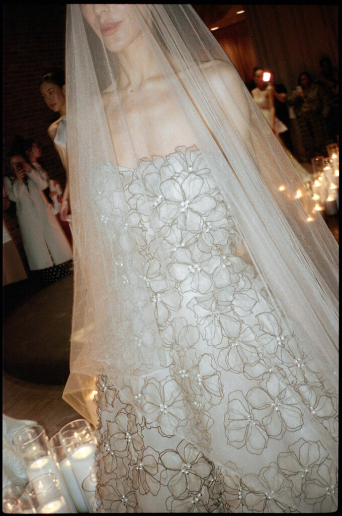 35mm film capture of a bride wearing a sheer veil over a gown with delicate floral embroidery and pearl details.