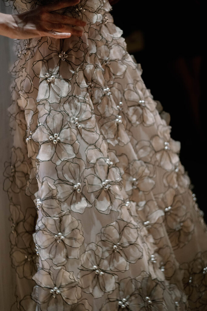 Close-up of hand-embroidered floral appliqués with pearl centers on a blush-toned sheer gown.