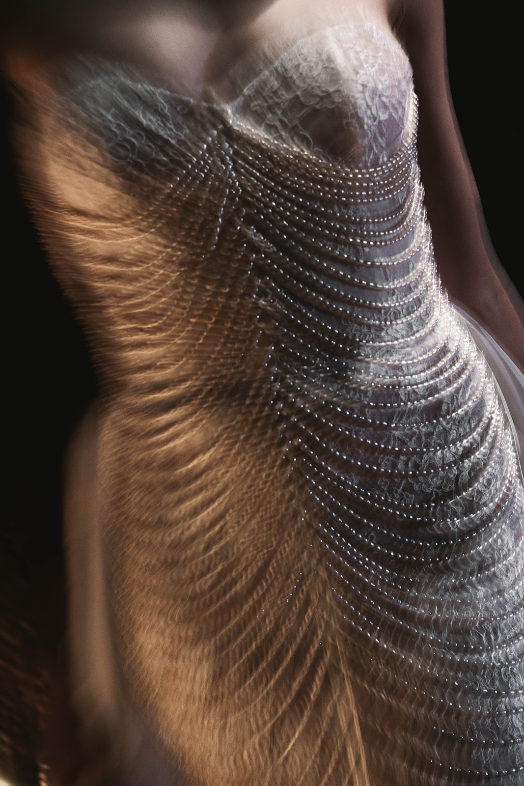 Close-up of a strapless lace bridal gown with cascading pearl draping, captured mid-motion to highlight fluidity and texture.
