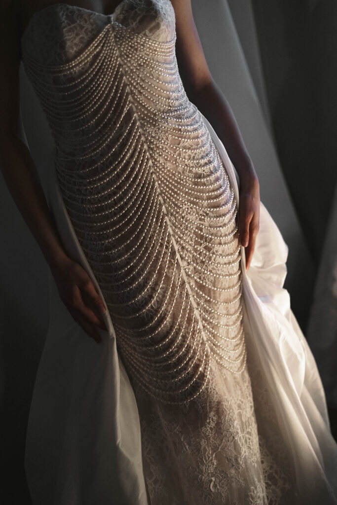 Full view of a lace gown with cascading pearl draping across the bodice and sheer overlay panels.