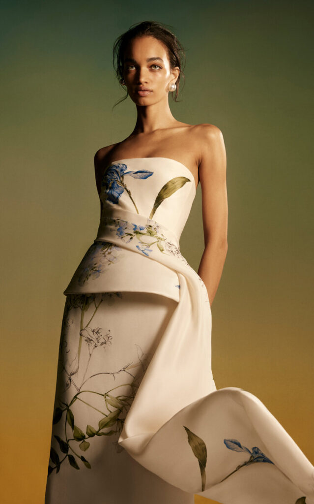 Ivory strapless gown with sculptural peplum and hand-illustrated blue botanical florals—merging soft structure with organic beauty in a dreamy garden-inspired silhouette.