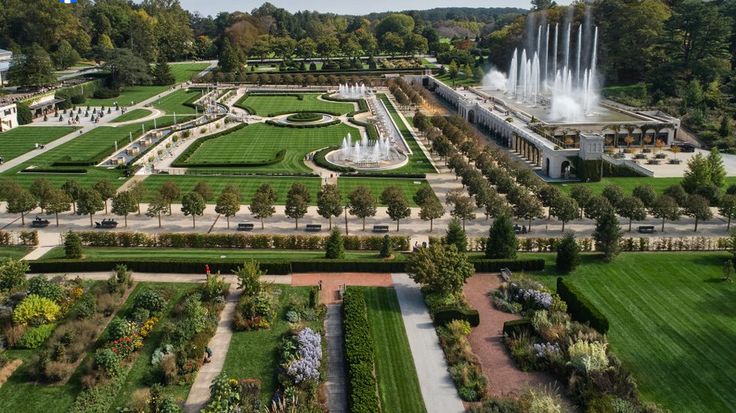 Aerial view of Longwood Gardens' formal landscape with symmetrical parterre gardens, water features, and dramatic fountains framed by tree-lined paths and lush greenery.