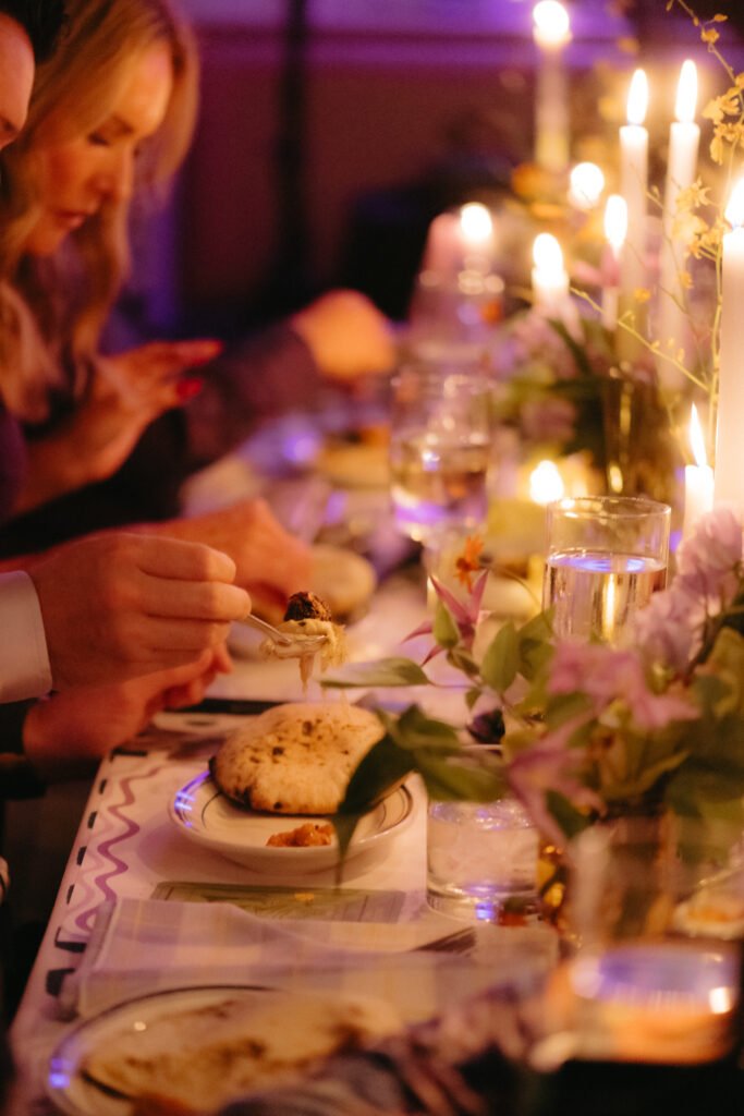 Close-up of a guest scooping food onto a plate during an intimate candlelit dinner, surrounded by florals and soft evening glow.