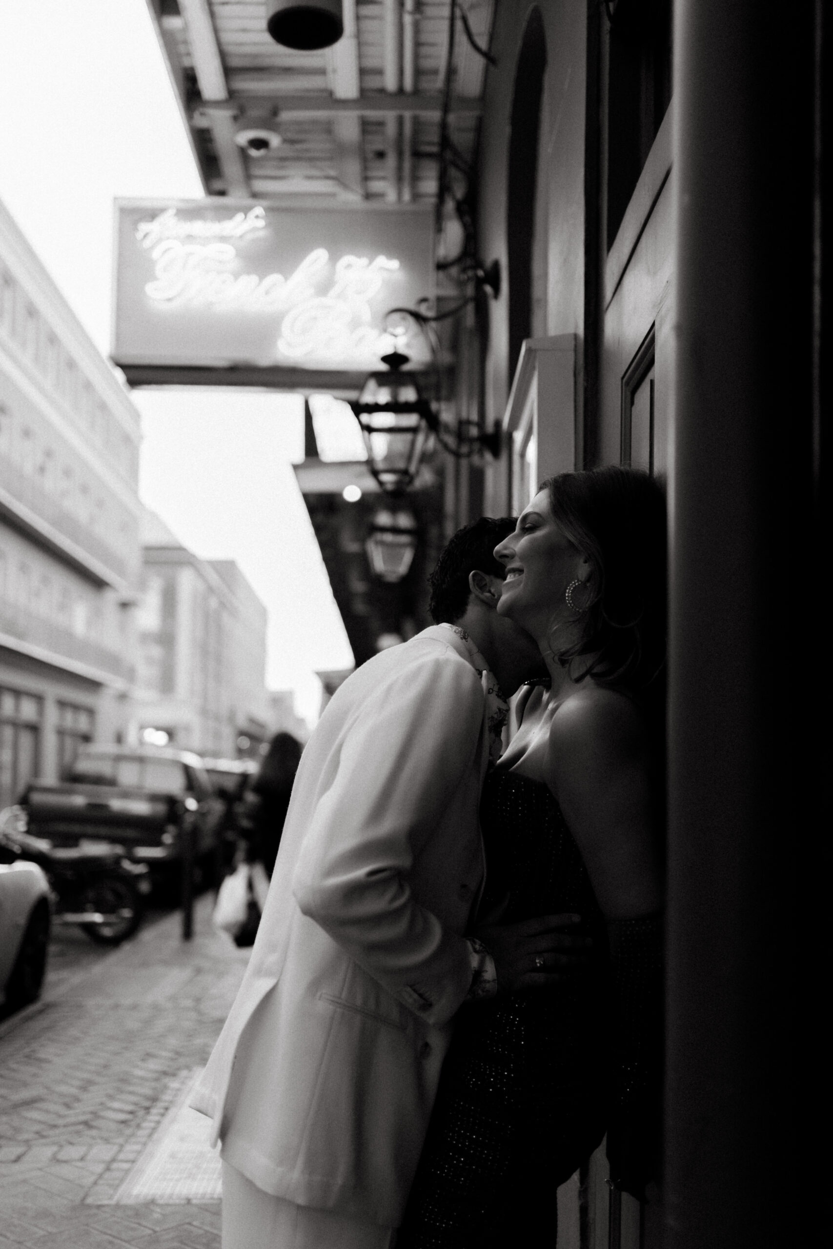 Black and white photo of a stylish couple embracing and laughing in a candid moment outside French 75 Bar in New Orleans—playful, magnetic, and full of chemistry.