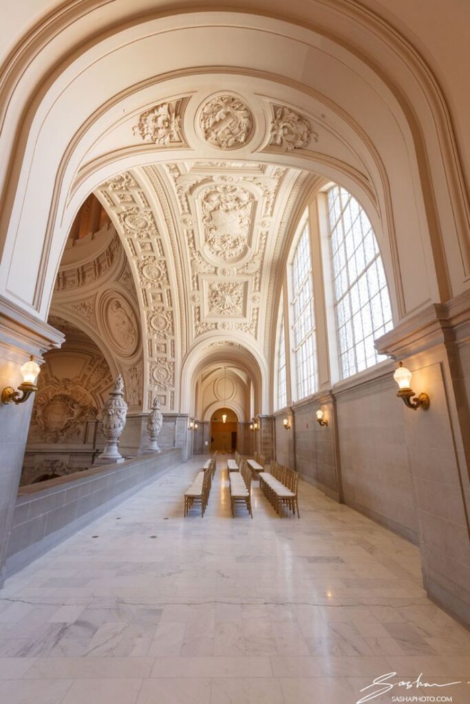Aisle setup with gold chairs beneath the elaborately sculpted ceiling of San Francisco City Hall's North Light Court, featuring neoclassical arches and intricate plasterwork.